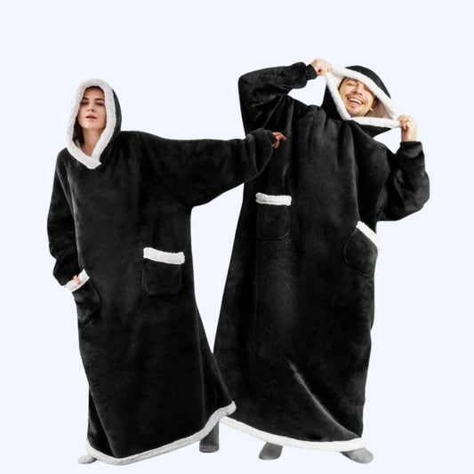 A man and a woman wearing matching black hoodie blankets with white faux-fur trim, standing against a light gray studio background.