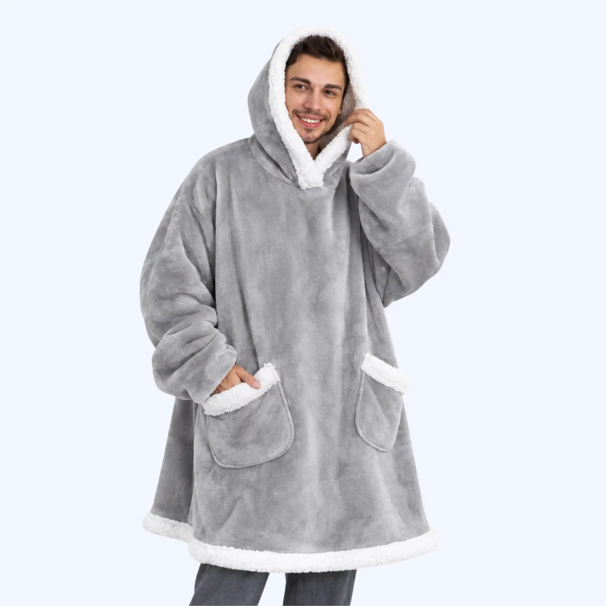 A man wearing a light grey hoodie blanket with white sherpa lining and two pockets. 
